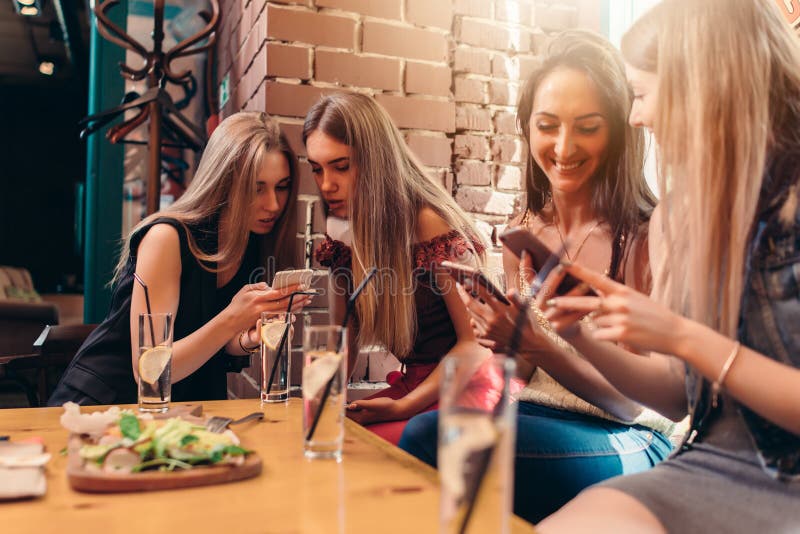Quattro studentesse sorridenti che si siedono nel self-service che chiacchiera facendo uso dei telefoni cellulari immagini stock libere da diritti Quattro studentesse sorridenti che si siedono nel self-service che chiacchiera facendo uso dei telefoni cellulari immagini stock libere da diritti
