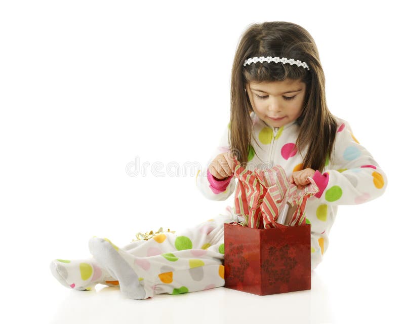 An adorable preschooler opening in Christmas gift in her colorful polka dot pajamas. On a white background. An adorable preschooler opening in Christmas gift in her colorful polka dot pajamas. On a white background.