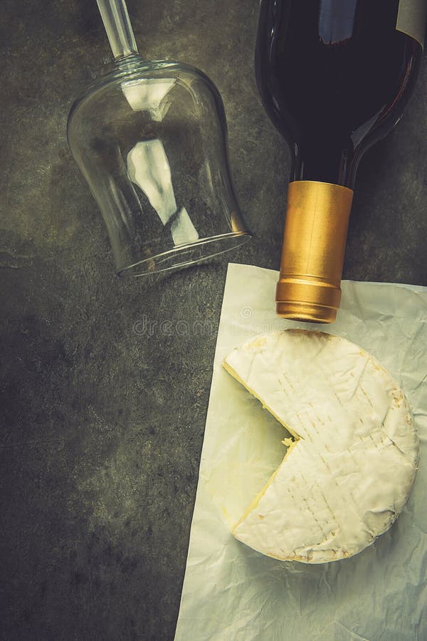 Queijo macio de Camambert do francês com a cunha cortada na garrafa de vinho de vidro vazia branca do papel de pergaminho no fund imagem de stock royalty free Queijo macio de Camambert do francês com a cunha cortada na garrafa de vinho de vidro vazia branca do papel de pergaminho no fund imagem de stock royalty free