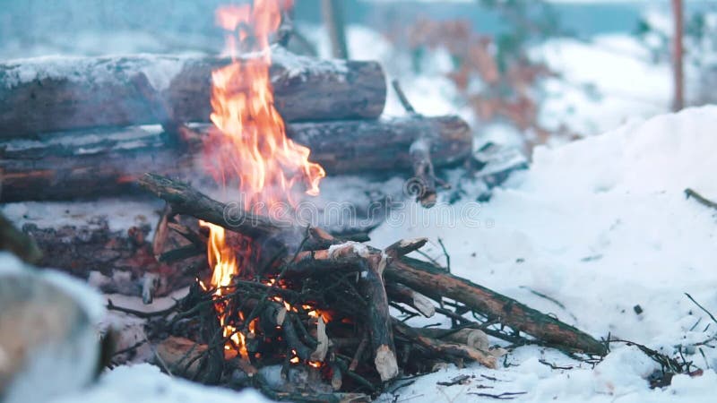 Queimaduras de Campfire na neve do morro da floresta, sobre um fundo de árvores cobertas de neve e montanhas queimando no inverno