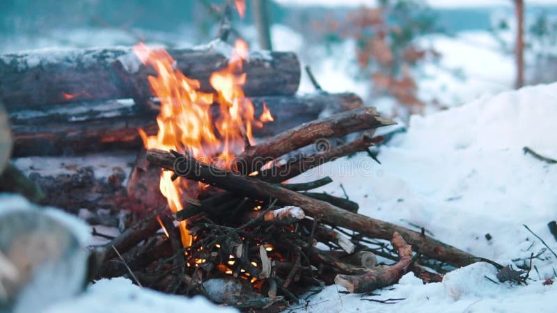 Queimaduras de Campfire na neve do morro da floresta, sobre um fundo de árvores cobertas de neve e montanhas queimando no inverno