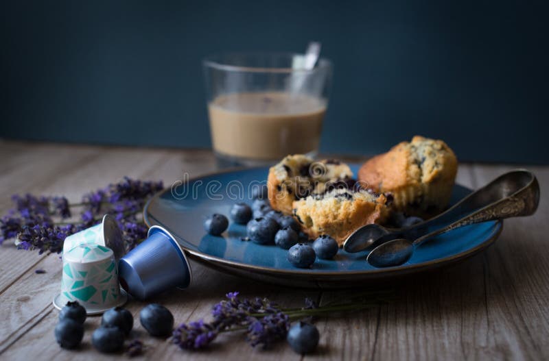 Moody dark food photo with a muffin and cranberries on a blue plate, nespresso capsules and a coffee cup in the background. Moody dark food photo with a muffin and cranberries on a blue plate, nespresso capsules and a coffee cup in the background