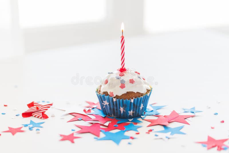 Independence day, celebration, patriotism and holidays concept - close up of glazed cupcake or muffin with burning candle and stars cofetti decoration on table at 4th july party. Independence day, celebration, patriotism and holidays concept - close up of glazed cupcake or muffin with burning candle and stars cofetti decoration on table at 4th july party