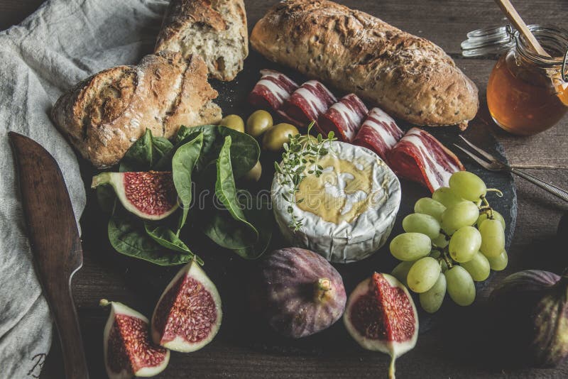 Queso del camembert, higos, jamon, miel y pan hecho en casa, en tablero oscuro de la porción sobre fondo de madera rústico imágenes de archivo libres de regalías Queso del camembert, higos, jamon, miel y pan hecho en casa, en tablero oscuro de la porción sobre fondo de madera rústico imágenes de archivo libres de regalías