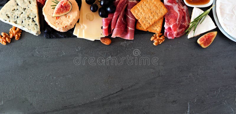 Quesos variados y aperitivos de carne, encima de ver el banner de la parte superior de la frontera sobre un fondo de piedra oscur imágenes de archivo libres de regalías