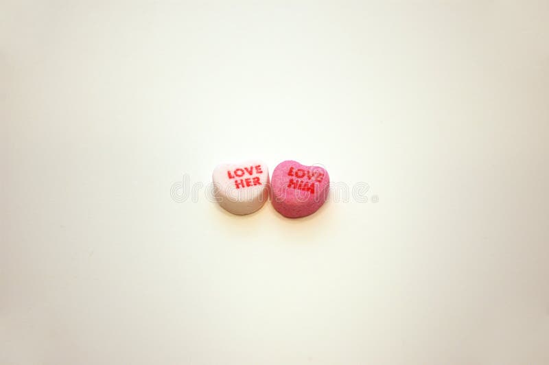 A pair of Valentines Day candy conversation hearts that say Love Her and Love Him. A pair of Valentines Day candy conversation hearts that say Love Her and Love Him