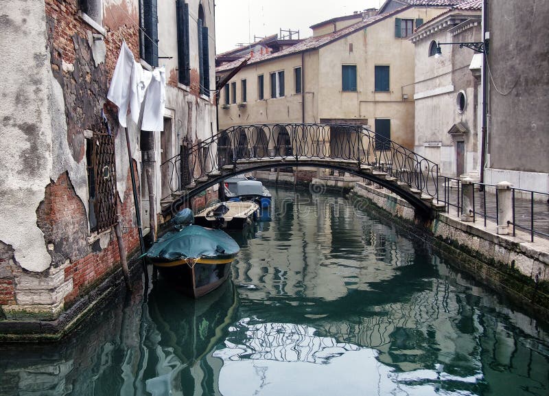 Quiet empty street in venice on a winter morning with a bridge crossing the canal and ancient buildings reflected in the water stock photo Quiet empty street in venice on a winter morning with a bridge crossing the canal and ancient buildings reflected in the water stock photo