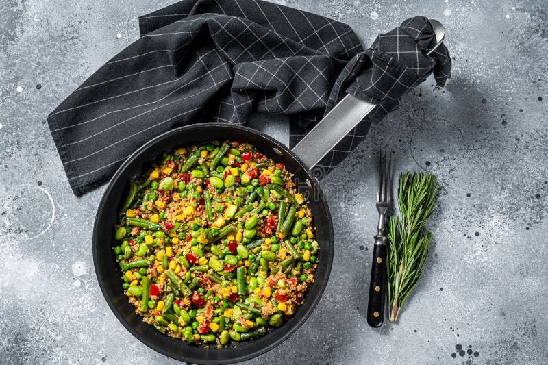 Quinoa salad with edamame, corn, carott, tomato, paprika, onions in a pan. Gray background. Top view