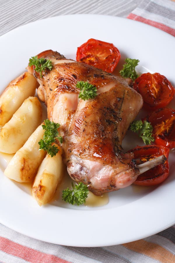 Rabbit leg roasted with apples and tomatoes on a plate closeup.