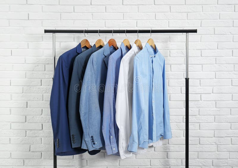 Rack with stylish men`s clothes near brick wall