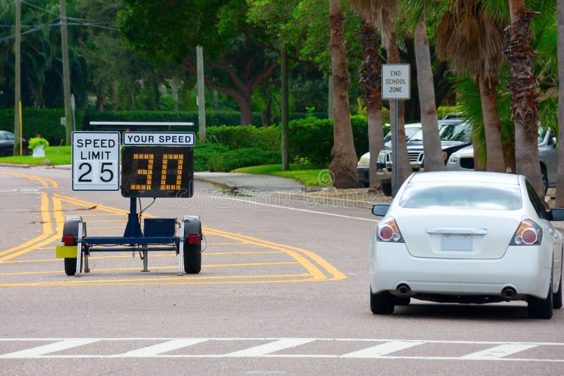 Radar speed limit indicator sign showing 30 proving a passing car is speeding as it drives down the road in a school zone