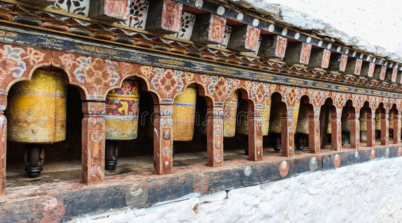 Raden av den traditionella gula buddistiska bönen rullar in väggen, Bhutan royaltyfri bild Raden av den traditionella gula buddistiska bönen rullar in väggen, Bhutan royaltyfri bild