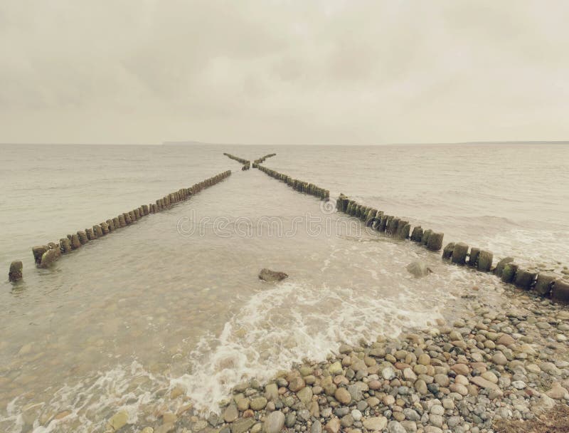 Raden av gamla trähögar som vågbrytaren framme av den steniga stranden royaltyfri fotografi Raden av gamla trähögar som vågbrytaren framme av den steniga stranden royaltyfri fotografi