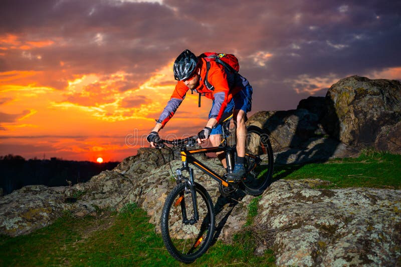 Cyclist Riding the Mountain Bike Down Spring Rocky Hill at Beautiful Sunset. Extreme Sports and Adventure Concept. Cyclist Riding the Mountain Bike Down Spring Rocky Hill at Beautiful Sunset. Extreme Sports and Adventure Concept.