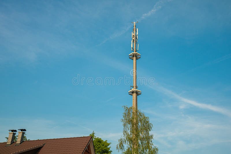 A radio mast for the mobile phone network towers above a residential building into the blue sky in a residential area