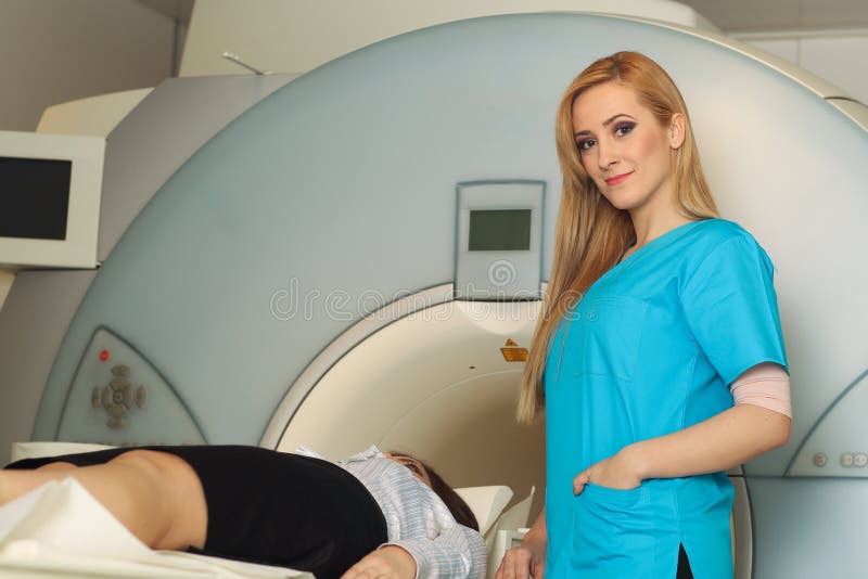 Radiologic technician smiling at mature female patient lying on a CT Scan bed working. Radiologic technician smiling at mature female patient lying on a CT Scan bed working