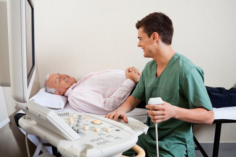 Young male radiologic technician smiling while looking at senior patient. Young male radiologic technician smiling while looking at senior patient