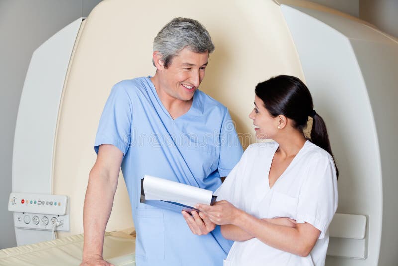 Multiethnic radiologic technicians smiling at each other while standing by MRI scan machine. Multiethnic radiologic technicians smiling at each other while standing by MRI scan machine