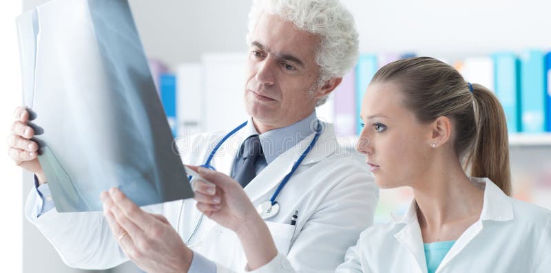 Radiologist checking an x-ray with his assistant in his office, healthcare and prevention concept. Radiologist checking an x-ray with his assistant in his office, healthcare and prevention concept