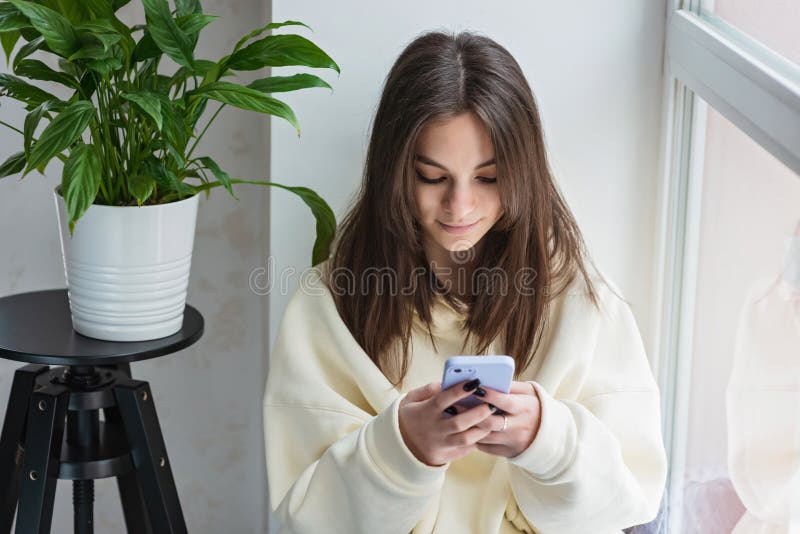 Radosna nastolatka patrząca na smartfona relaksującego się w domu ciesz się korzystaniem z aplikacji mobilnych online grających w. Radosna nastolatka, patrząca na relaks smartfona w domu, cieszy się korzystaniem z aplikacji mobilnych online grających w gry na telefonach komórkowych, sprawdzających wiadomości lub wiadomości z mediów społecznościowych. miękka selektywna koncentracja
