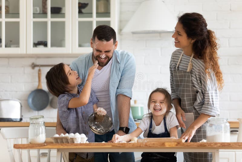 Radosni rodzice z małymi dziećmi bawią się gotować w kuchni