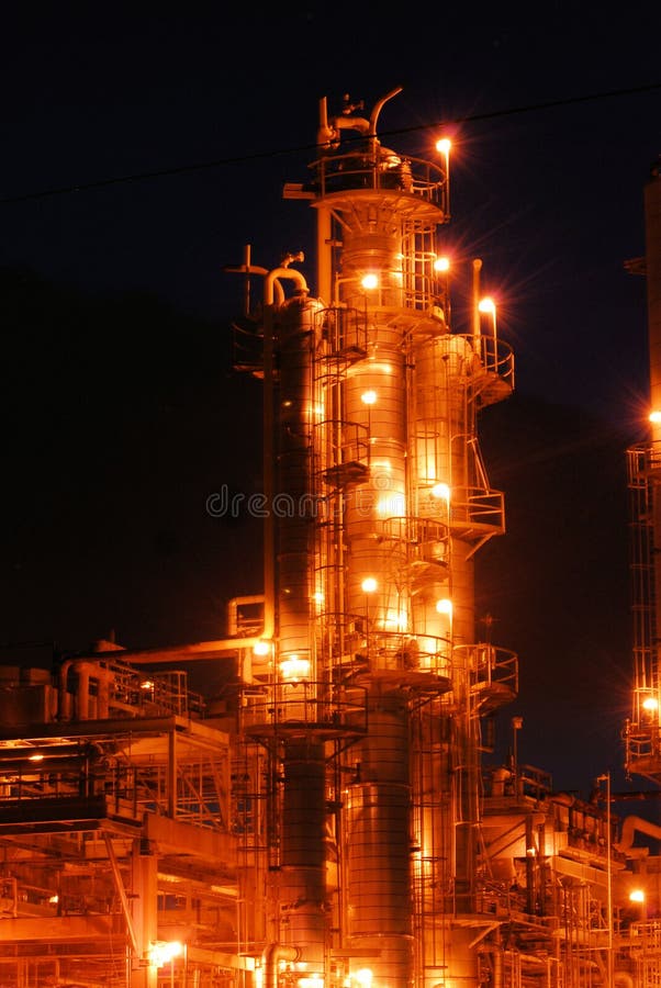 A column in an oil refinery in operation with columns, tanks, and piping against a night sky. A column in an oil refinery in operation with columns, tanks, and piping against a night sky.