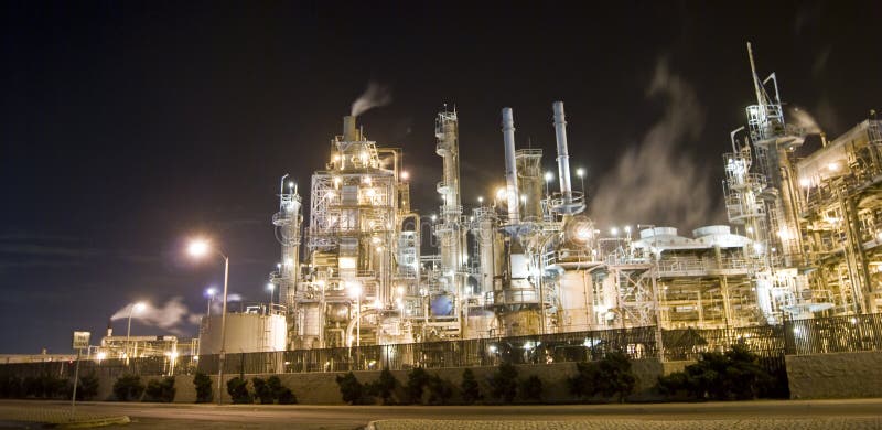 An oil refinery in the United States with a series of foggy and smoky stacks. Night image of an industrial complex. An oil refinery in the United States with a series of foggy and smoky stacks. Night image of an industrial complex.