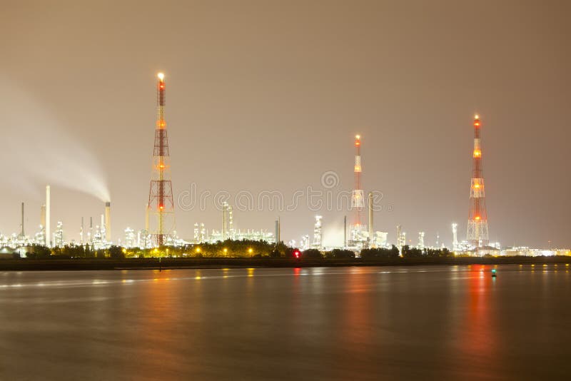 An oil refinery with tall gas flare stacks in a harbor with dirty night sky. An oil refinery with tall gas flare stacks in a harbor with dirty night sky.