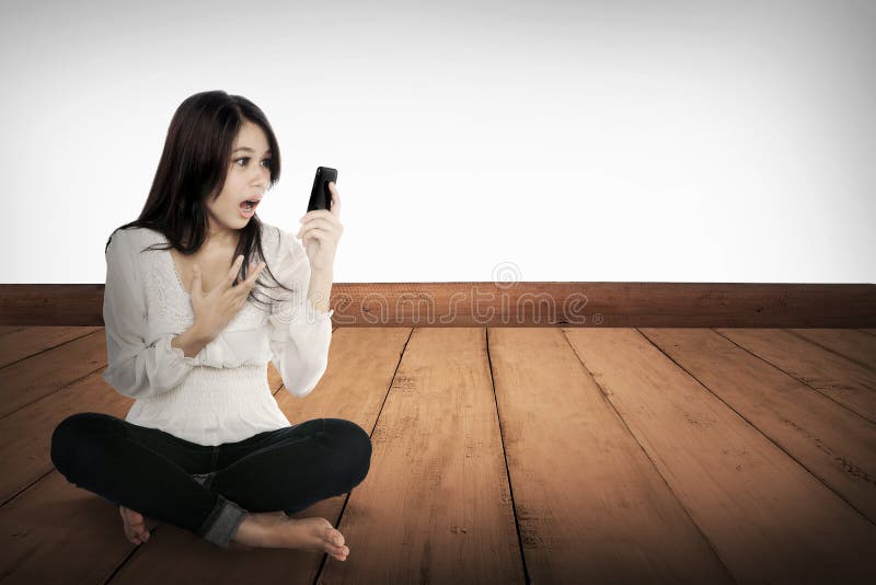 Ragazza abbastanza asiatica che per mezzo del cellulare sul pavimento di legno fotografia stock Ragazza abbastanza asiatica che per mezzo del cellulare sul pavimento di legno fotografia stock