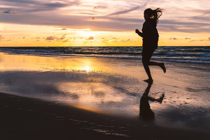 Ragazza adolescente che corre scalzo su una spiaggia sabbiosa al tramonto - una foto silenziosa di una giovane donna contro il ci fotografie stock libere da diritti Ragazza adolescente che corre scalzo su una spiaggia sabbiosa al tramonto - una foto silenziosa di una giovane donna contro il ci fotografie stock libere da diritti