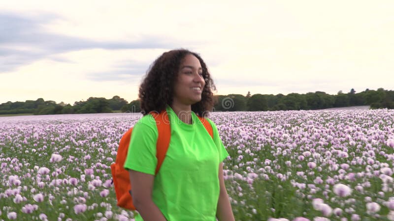 Ragazza afro-americana di razza mista, giovane donna, che fa escursionismo nel campo dei fiori di papavero rosa