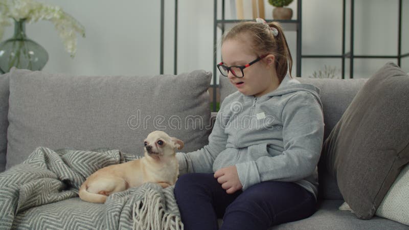 Ragazza allegra con sindrome di Down rilassata con un animale domestico al chiuso video d archivio