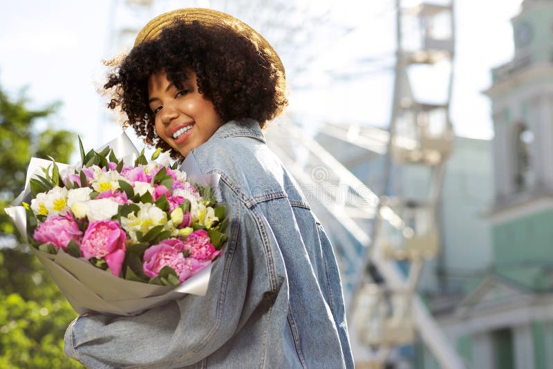 Ragazza allegra in fiori della tenuta del cappello di paglia immagini stock libere da diritti
