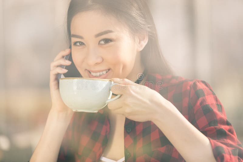 ragazza asiatica attraente che per mezzo dello smartphone e bevendo caffè in caffè del caffè immagini stock libere da diritti ragazza asiatica attraente che per mezzo dello smartphone e bevendo caffè in caffè del caffè immagini stock libere da diritti