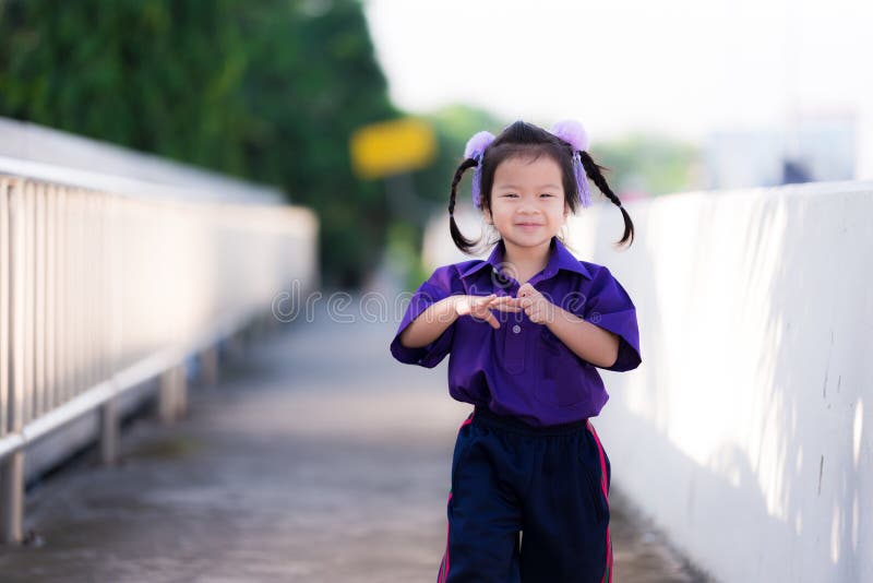 Ragazza asiatica con un sorriso dolce. il bambino indossava una camicia viola di ginnastica e pantaloni neri di lana. studentessa immagine stock