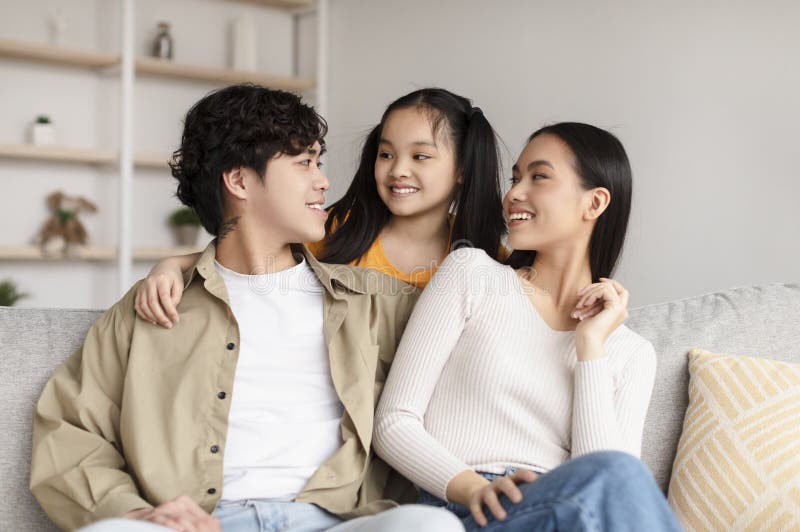 Ragazza asiatica sorridente abbraccia madre e padre sul divano che comunicano e si divertono fotografie stock libere da diritti