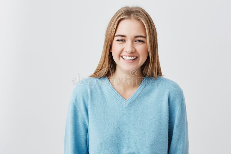 Ragazza attraente spensierata con capelli biondi, occhi scuri che portano maglione blu sciolto sorridente felicemente nella macch immagine stock libera da diritti Ragazza attraente spensierata con capelli biondi, occhi scuri che portano maglione blu sciolto sorridente felicemente nella macch immagine stock libera da diritti