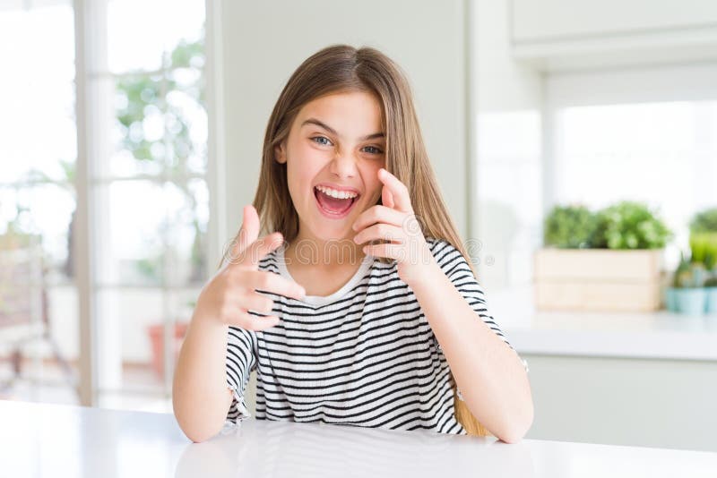 Ragazza bellissima con una camicia a strisce che punta le dita alla telecamera con una faccia felice e divertente fotografia stock