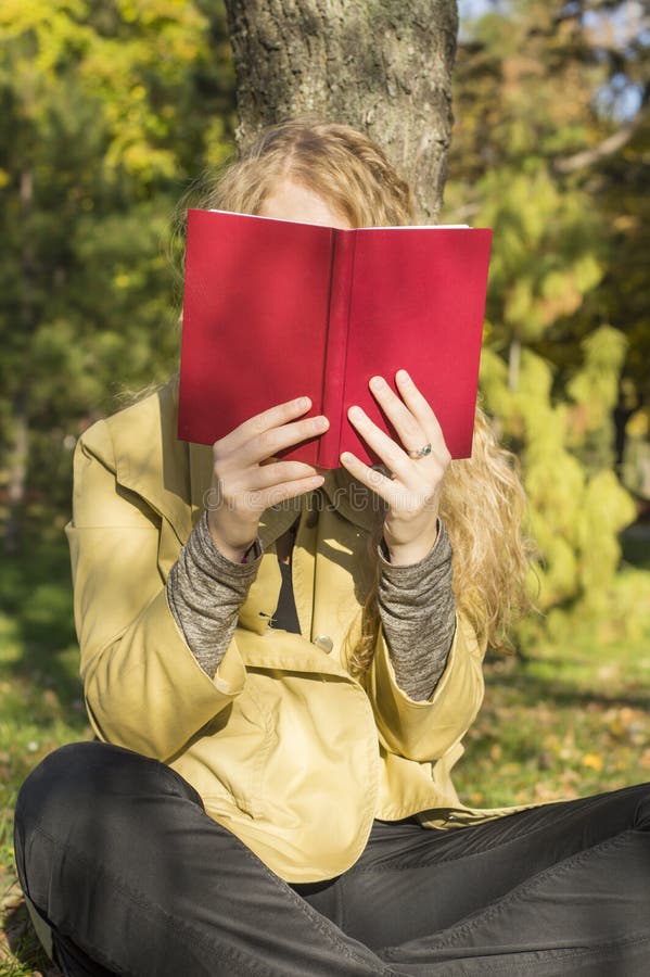 Ragazza bionda che legge un libro in un parco un giorno soleggiato immagine stock libera da diritti Ragazza bionda che legge un libro in un parco un giorno soleggiato immagine stock libera da diritti