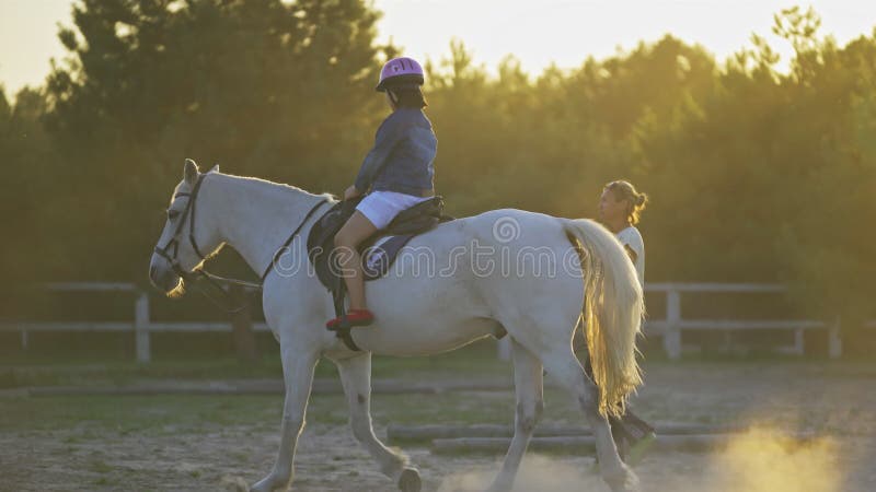 Ragazza cavalcatrice su un cavallo bianco con un istruttore di equitazione. una bambina impara con un istruttore a cavallo a ranch