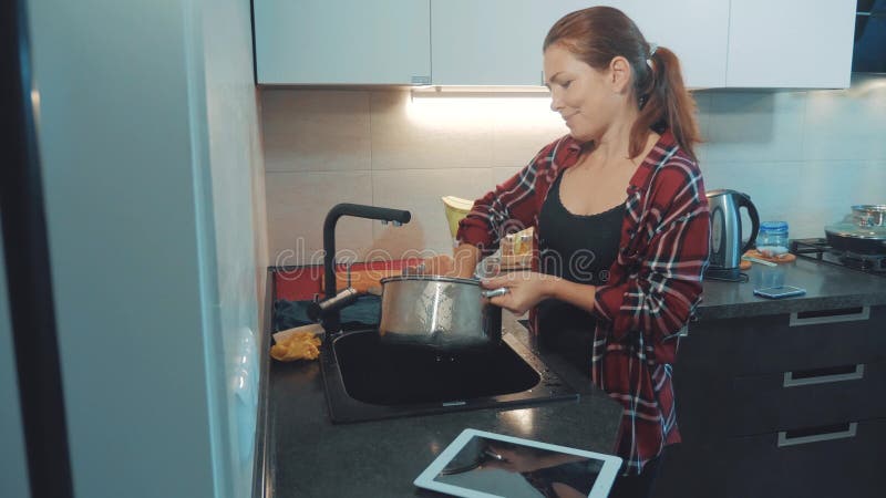 Ragazza che lava i piatti nel tagliere della cucina che esamina una compressa digitale Cuochi della donna nella cucina la ragazza