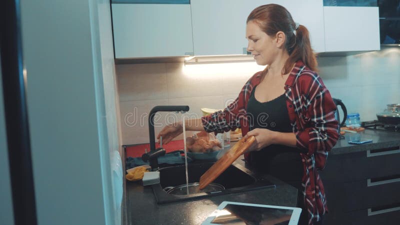 Ragazza che lava i piatti nel tagliere della cucina che esamina una compressa digitale Cuochi della donna nella cucina la ragazza