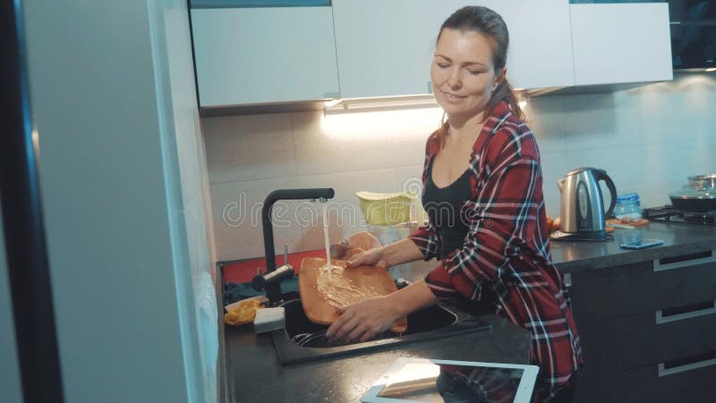 Ragazza che lava i piatti nel tagliere della cucina che esamina una compressa digitale Cuochi della donna nella cucina la ragazza