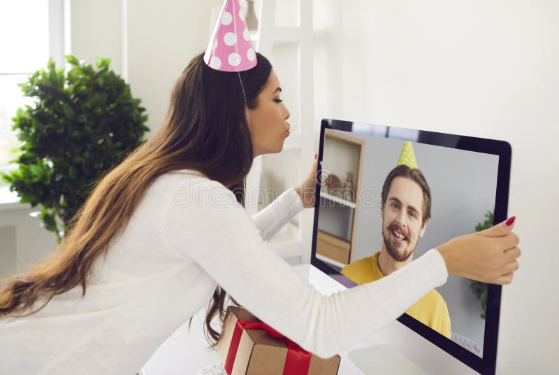 Ragazza che organizza una festa di compleanno online con il suo ragazzo e bacia lo schermo del computer immagine stock libera da diritti