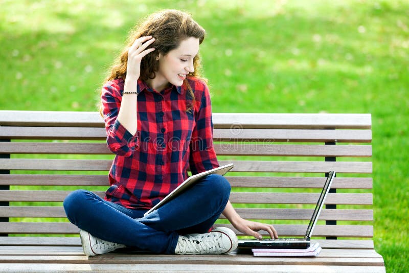 Ragazza che per mezzo di un computer portatile su un banco fotografie stock libere da diritti Ragazza che per mezzo di un computer portatile su un banco fotografie stock libere da diritti