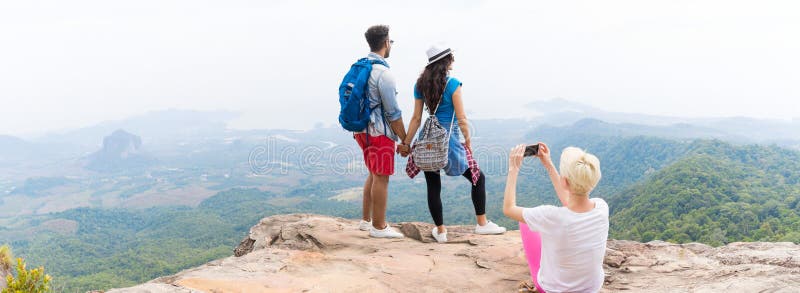 Ragazza che prende foto delle coppie con gli zainhi che posano sopra il paesaggio su panorama dello Smart Phone delle cellule, gi immagine stock libera da diritti Ragazza che prende foto delle coppie con gli zainhi che posano sopra il paesaggio su panorama dello Smart Phone delle cellule, gi immagine stock libera da diritti