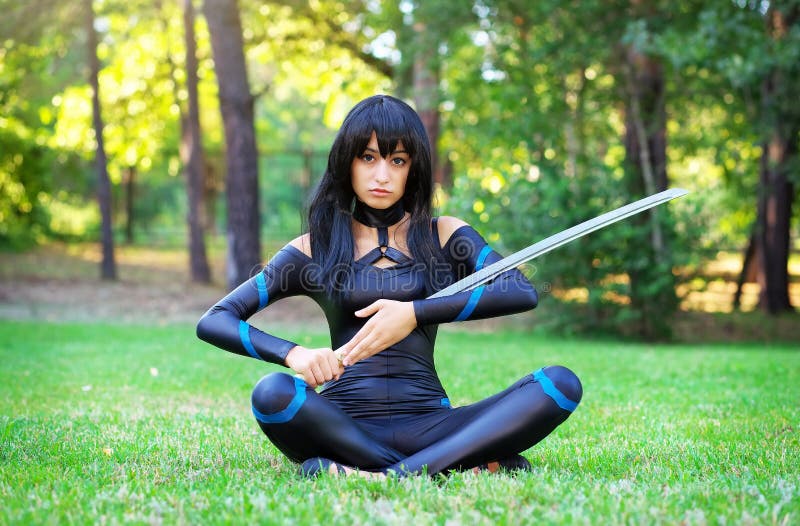 Ragazza che si siede sull'erba e che tiene la spada del samurai fotografia stock libera da diritti Ragazza che si siede sull'erba e che tiene la spada del samurai fotografia stock libera da diritti