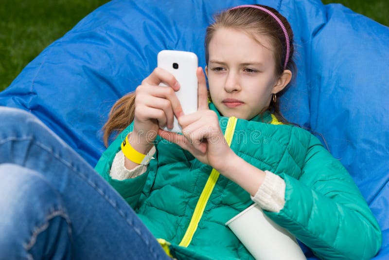 Ragazza con il telefono cellulare all'aperto in Bean Bag Chair fotografia stock Ragazza con il telefono cellulare all'aperto in Bean Bag Chair fotografia stock