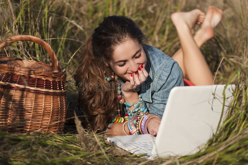 Ragazza dai capelli lunghi che si trova al computer portatile ed a sorridere immagine stock libera da diritti Ragazza dai capelli lunghi che si trova al computer portatile ed a sorridere immagine stock libera da diritti