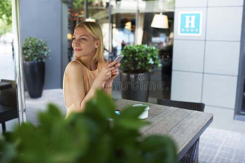 Ragazza dei pantaloni a vita bassa che chiacchiera sullo Smart Phone nel terrazzo della caffetteria del marciapiede immagine stock Ragazza dei pantaloni a vita bassa che chiacchiera sullo Smart Phone nel terrazzo della caffetteria del marciapiede immagine stock